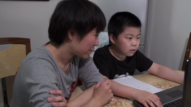Chinese kid and mother doing online schooling at home amid coronavirus pandemic