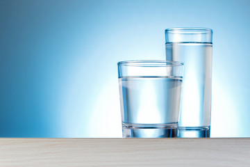 Two Glass Of Water On Table Against Blue Background With Copy Space. Concept Clean Water.
