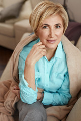 Mature Woman. Beautiful Healthy Middle Age Female Sitting On Sofa At Home. Beauty And Comfort Concept.
