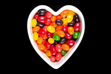 Assorted colorful jelly beans, sweet candy background with a heart-shaped bowl isolated on black. Kids' junk food.