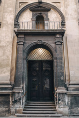 Fototapeta premium Antique baroque brown carved door and balcony by decorative stucco on a beige wall with capitals. Facade of the Jesuit Church in Lviv.
