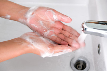 Hands of woman wash their hands in a sink with foam to wash the skin and water flows through the hands. Concept of health, cleaning and preventing germs and coronavirus from contacting hands