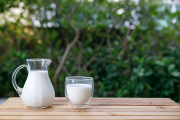 jug and cup of milk on a wooden table at green tree background