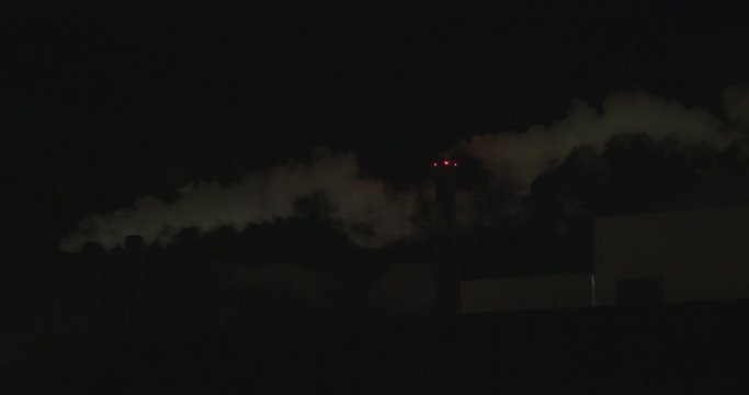 Dramatic night shot of white smoke eminating from a factory chimney with red lights shining through the smog