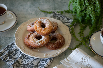 Doughnuts and a cup of tea or coffee with green plants and white linen