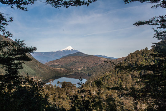 a picture of a volcanic, mountains and a lake from behind trees