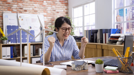 Happy young emotional entrepreneur woman feeling excited of working process making job great indoors. successful smiling asian chinese female engineer in spectacles sitting at desktop in workplace