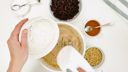 Chocolate Chip Cookies recipe. Chef adds flour into a cookie batter, close up on white background, view from above
