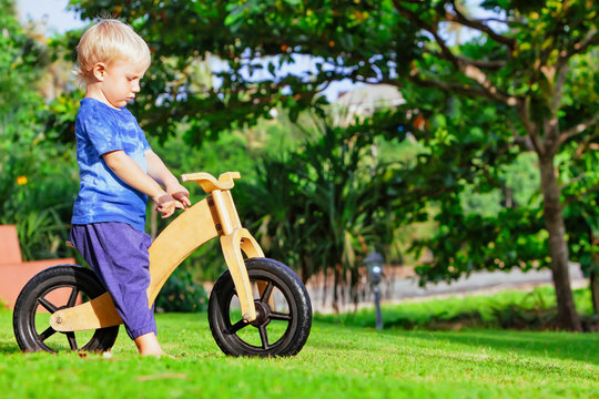 2 - 3 years joyful boy riding a wooden balance bike (run bike). Happy barefoot child learning to wheel, keep balance on training bicycle in the garden. Active kid playing outside. First day on bike.