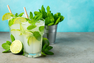 Two homemade lemonade or mojito cocktail with lime, mint and ice cubes in a glass on a light stone table. Fresh summer drink. With copy space.