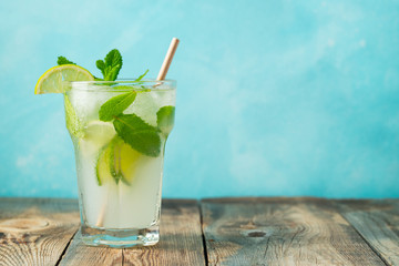 homemade lemonade or mojito cocktail with lime, mint and ice cubes in a glass on a wooden rustic table. Fresh summer drink. with copy space.