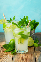 Two homemade lemonade or mojito cocktail with lime, mint and ice cubes in a glass on a wooden rustic table. Fresh summer drink.