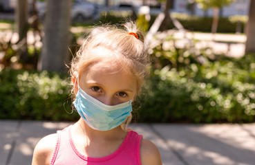 A little girl walks in the park in a medical face mask. A little girl walks through an empty city and covers her face with a mask from a coronavirus. Quarantine due Coronavirus time. Copy Space.
