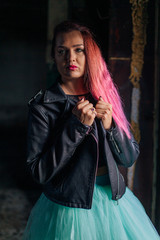 Portrait of a young girl with pink hair standing next to the old rusty door inside of collapsed building surrounded by ruins