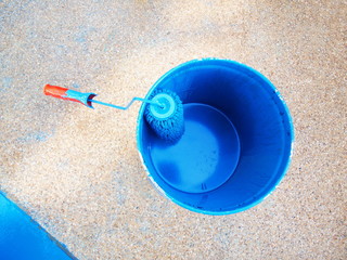 Blue paint bucket with brush rollers For painting cement floor surfaces On a cement floor background. Selective focus