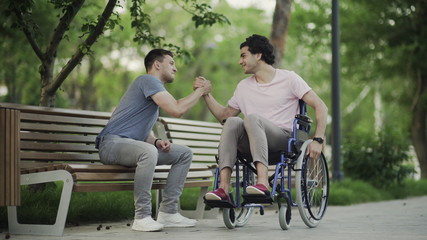 Young man in a wheelchair meet his friend in the park.