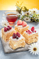 Delicious layer cake Napoleon decorated with berries and powdered sugar on a gray stone Board on a gray-yellow background, vertically