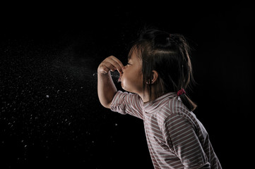 Kid of sneezing, coughing, shocking food concept. A little Asian girl of 7 years old covered nose while sneezing and Causing the water to flow out of the mouth with black background.