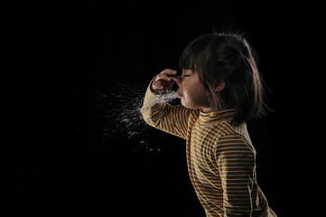 Kid of sneezing, coughing, shocking food concept. A little Asian girl of 5 years old covered nose while sneezing and Causing the water to flow out of the mouth with black background.