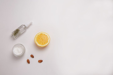 On a white background micellar water, white cream, almonds and a slice of lemon.