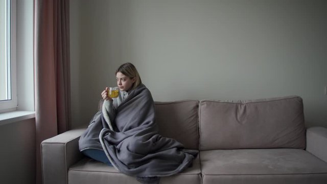 The quarantined girl wrapped in a gray plaid drinks hot tea. Treatment for acute respiratory infections, flu, bronchitis.