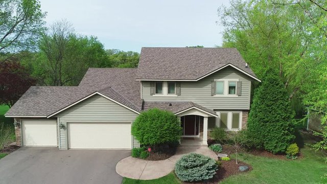 Drone aerial of a middle class suburban American home with typical modern design, a nice lawn and garage, filmed on a sunny summer or spring day.