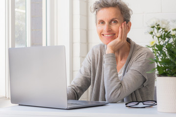 Close up of middle age woman with laptop smiling at camera - working from home concept (selective focus)