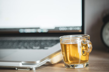 Aromatic hot tea in a tea glass on the computer table. People working from home concept with a cup of tea on the table with copy space close up. Relaxing from working by drinking a hot beverage.