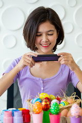 Asian young pretty woman enjoy taking a photo to the colorful fantasy Easter egg by using smartphone. Colorful fancy Easter egg in bucket. The symbolic of Easter egg festival concept.