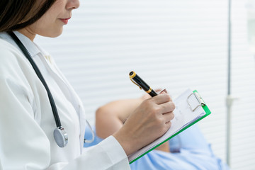 Specialist doctor in hospital noting a patients' examination result into notepad close up. Asian woman patient having health disease and worried about her health, doctor giving a consulting to patient