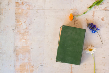 Closed green book and flowers on old wooden desk backgroud with copy space.
