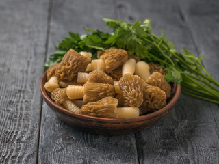 A bowl of morels with parsley leaves on a wooden background.