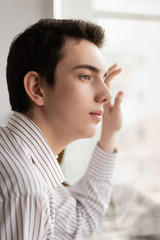 Pensive guy looking out window at home