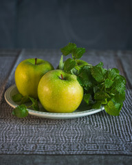 Green apples with a bunch of lemon balm on a ceramic green plate
