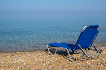 Fototapeta na wymiar Blue lonely deck chair on the sea beach. Sunny day, Halkidiki, Greece.