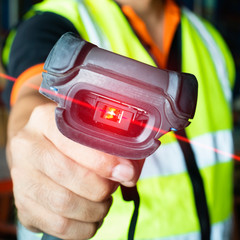 close up bar code scanner, warehouse worker holding bar code scanner with scanning red laser, warehouse equipment and inventory management.