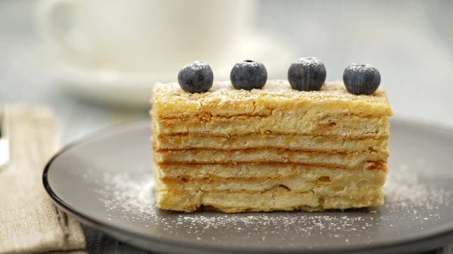 Cream puff pastry cake, decorated with four blueberries, is being powdered with icing sugar. UHD
