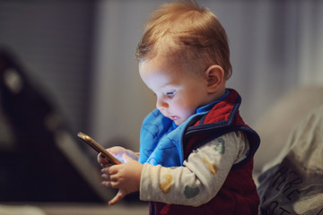 Portrait of cute blond toddler sitting in mother's lap, holding smart phone and touching screen. He...