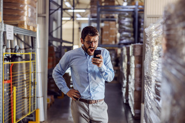 Angry businessman having phone conversation and shouting while standing in warehouse.