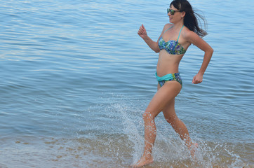 Running athletic young girl in a swimsuit runs along the beach. Healthy slim body and athletic figure