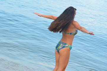 A young girl on the sea spreads her arms to the side and enjoys freedom