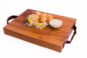 Shrimp skewers in coconut curry and Asian sauce on a wooden board on a white background