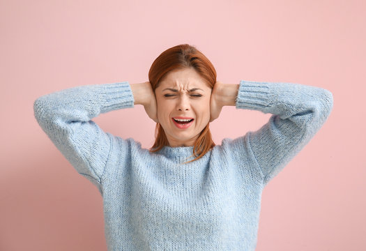 Young woman suffering from loud noise on color background