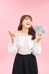 Portrait of young asian woman showing bunch of money banknotes on pink background