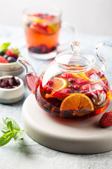 Fruit red tea with berries in glass teapot on white background