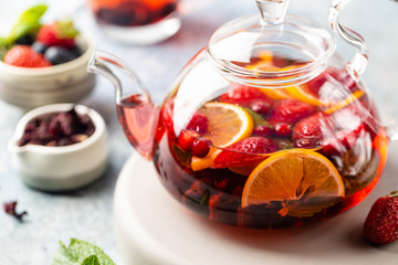 Fruit red tea with berries in glass teapot on white background