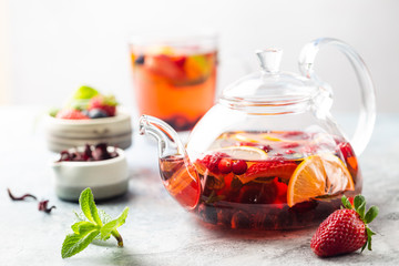 Fruit red tea with berries in glass teapot on white background