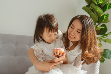 Mommy and kid daughter eating donut when sitting on sofa at home