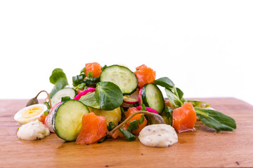 Salad with red fish, fresh vegetables - cucumber and radish, capers, egg, herbs, olives and sauce on a wooden tray, board, dish. The object is isolated on a white background.