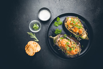 Baked aubergine or eggplant boats stuffed with mushrooms, vegetables and cheese on black background, top view